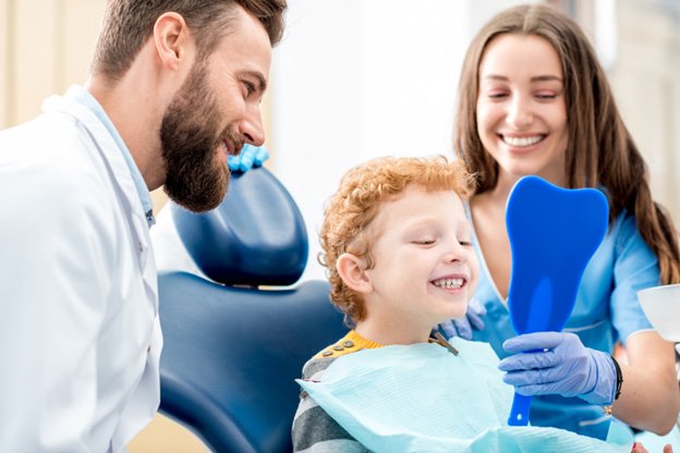 Child sitting in dental chair looking in a mirror smiling